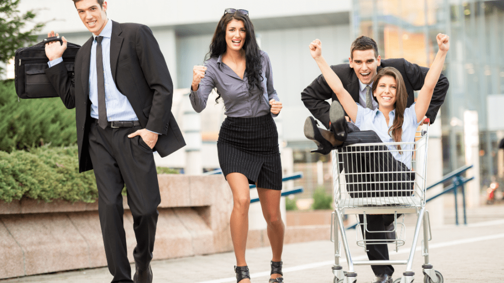 Men and women smiling, girl sitting in the shopping cart while man is pushing the cart